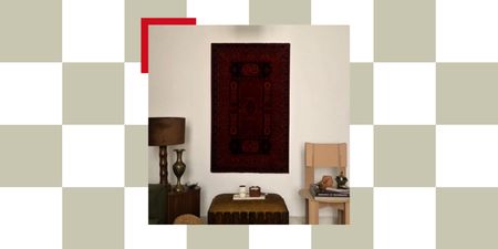 prayer mat mounted on wall in living room with lamp, ottoman, and seat with books and trinkets on it