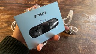 FiiO CP13 held in a hand, above an antique wooden table