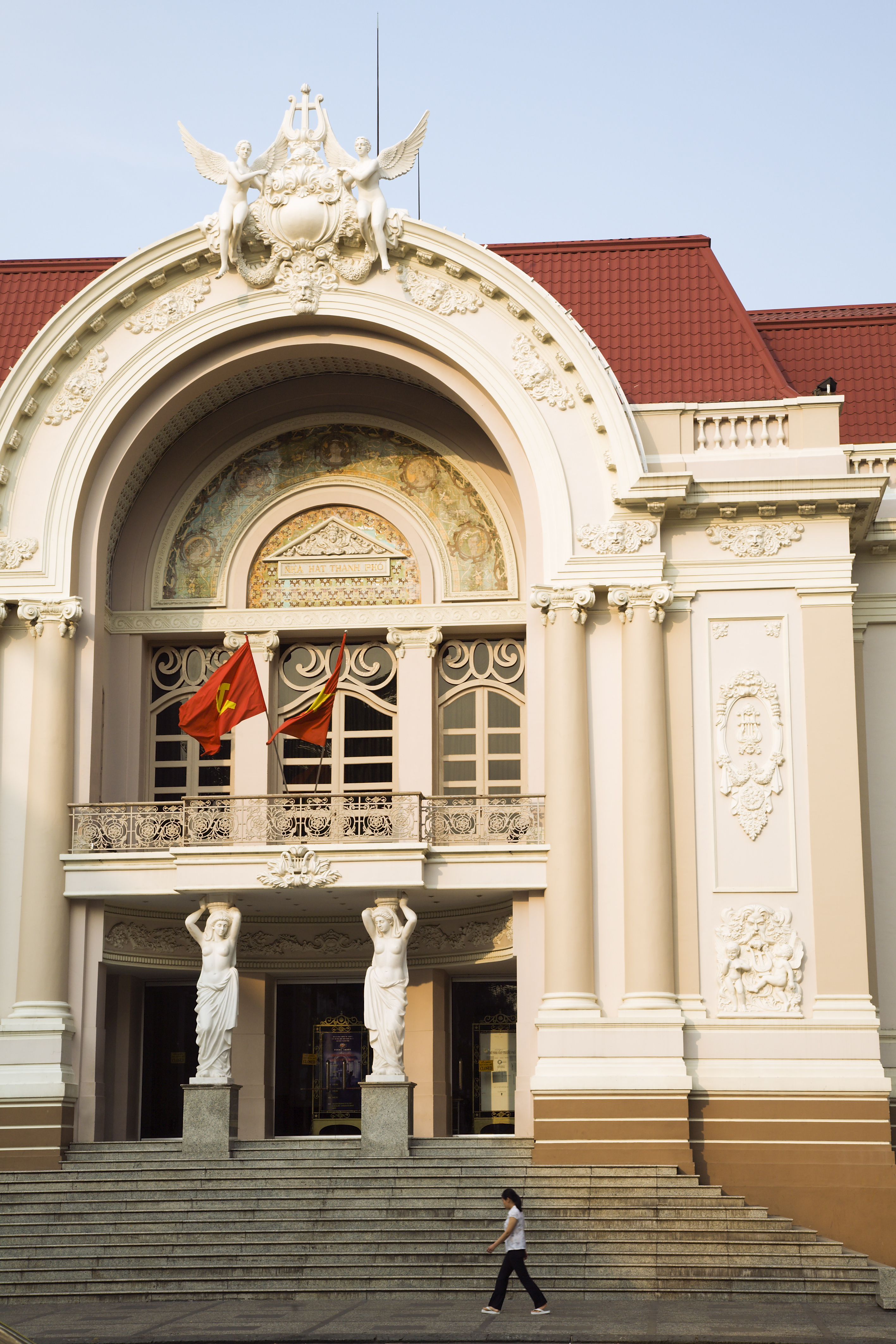 Outside view of a historical building with an arched, stuccoed facade illuminated by natural sunshine and with a red flag flowing midair.