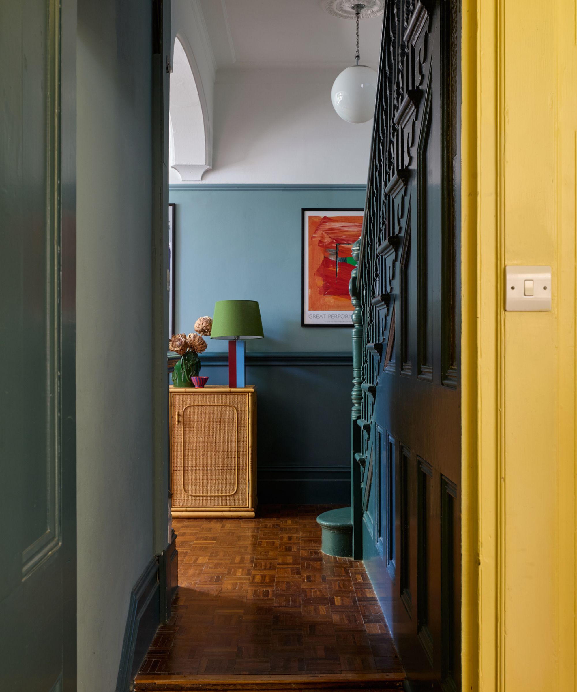 a blue entryway with a green lamp and parquet wooden floor. a glimpse of yellow is seen through the doorway.