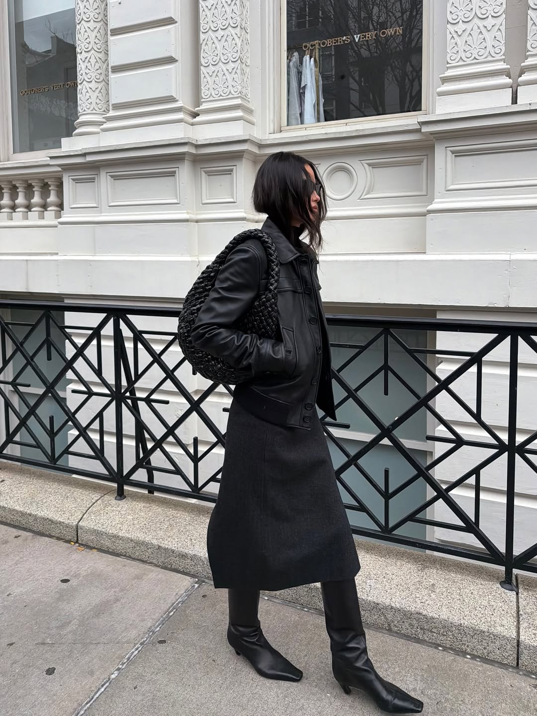 A woman wears a black knee-length skirt and boots