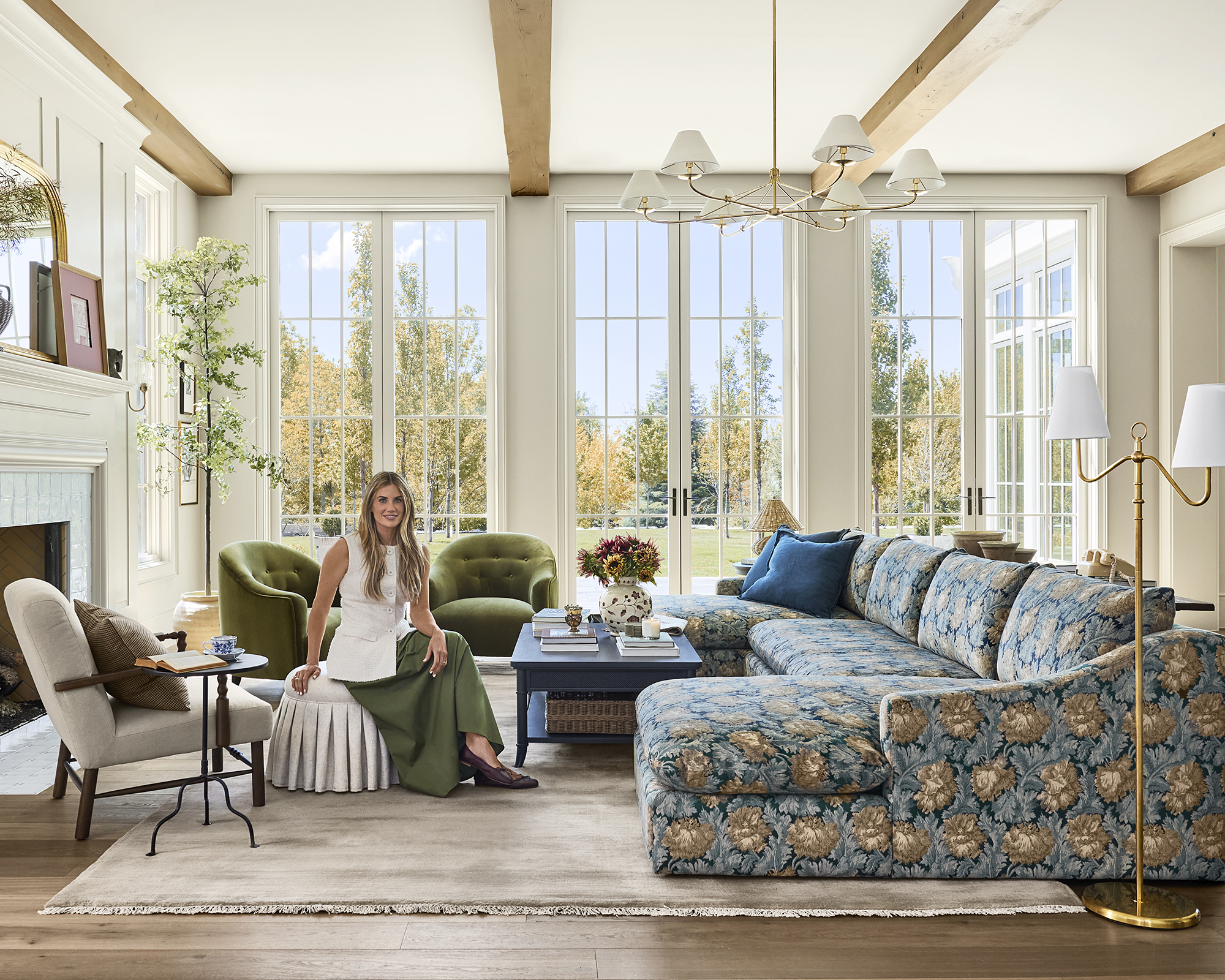Shea McGee in a white top sat in a large living room next to a floral couch
