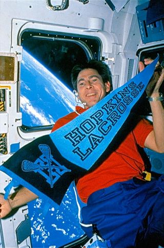STS-35 payload specialist Samuel Durrance floats with a Hopkins Lacrosse pennant aboard space shuttle Columbia in 1990.