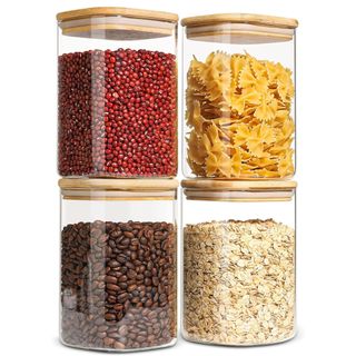 Four square glass containers with wooden lids are stacked up and filled with dry foods