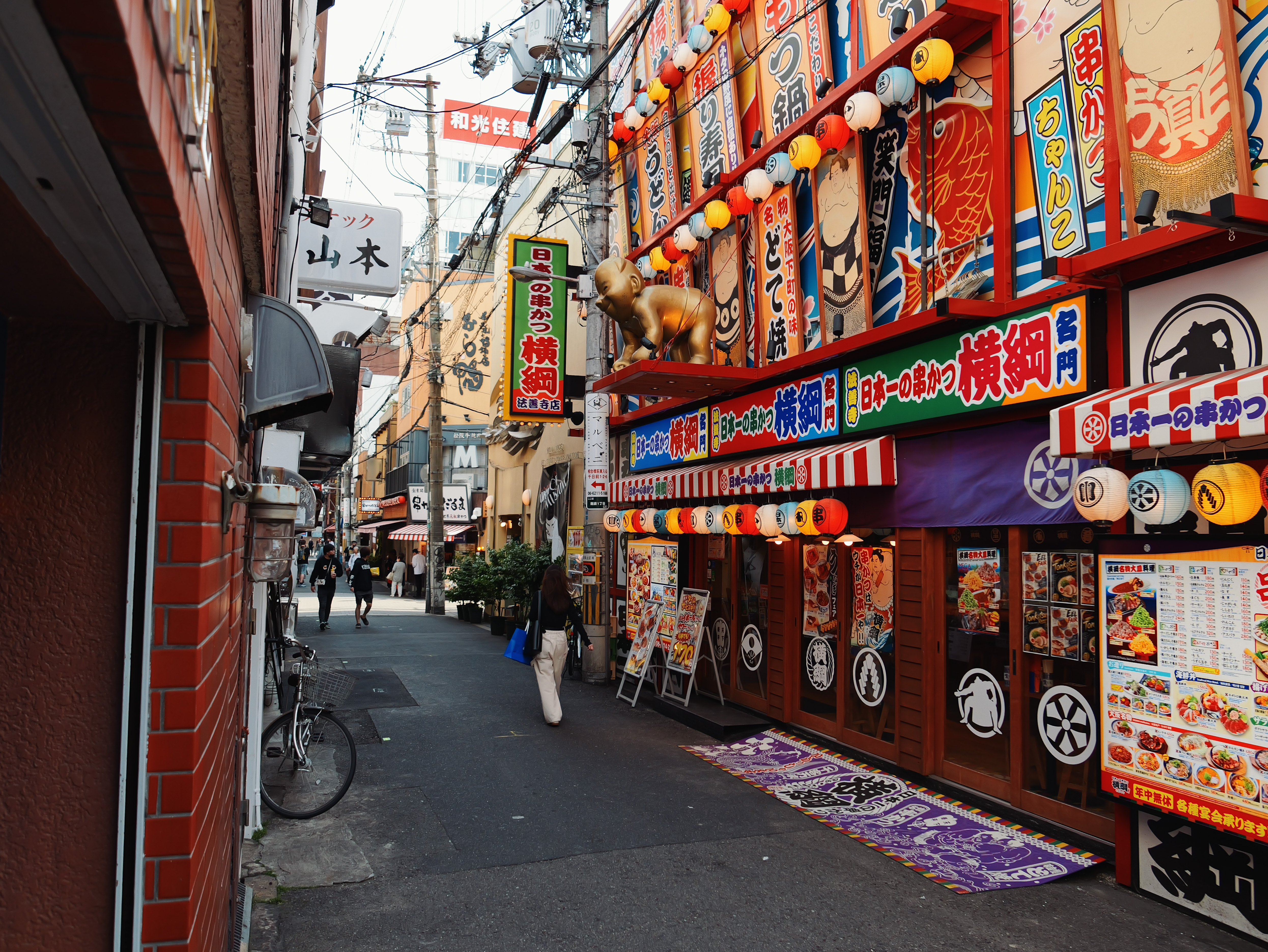Brightly colored restaurant signs and lanterns on a street in Osaka.
