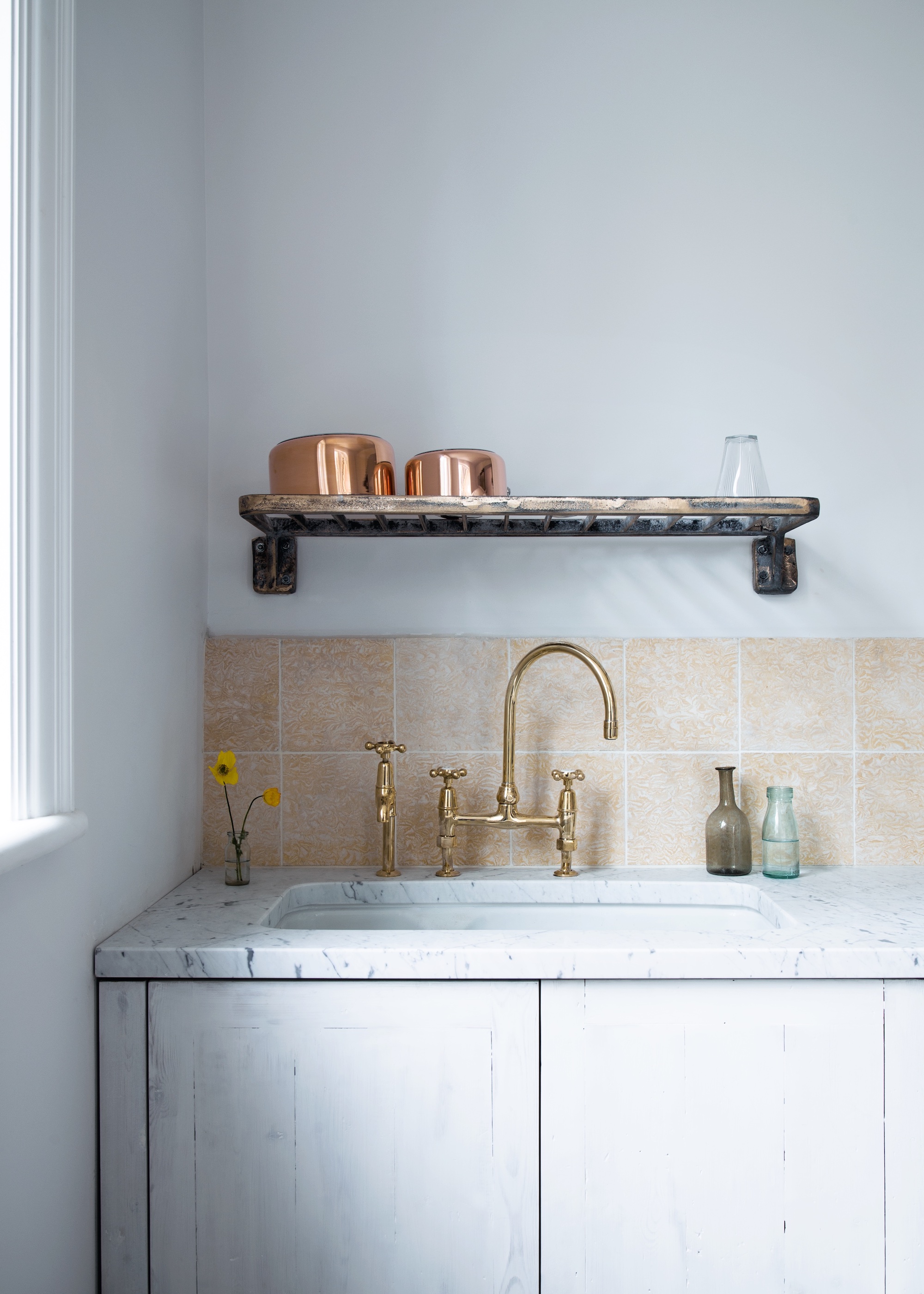 kitchen with sink and metal rack above with pots and glassware on top. On the counter is a small plant and other glass accessories