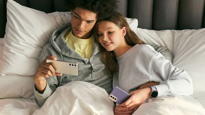 Samsung Galaxy S21 Android phone being held by a man and a woman in bed
