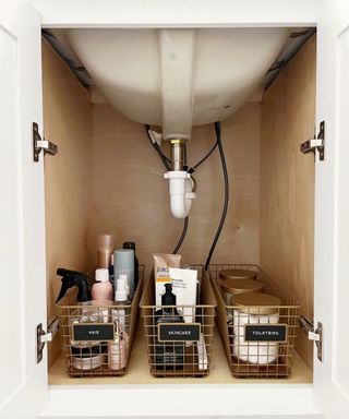 Gold colored metal under sink storage baskets with toiletries and black labels