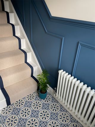 A hallway with blue half-wall panelling and stair panelling and patterned floor tiles