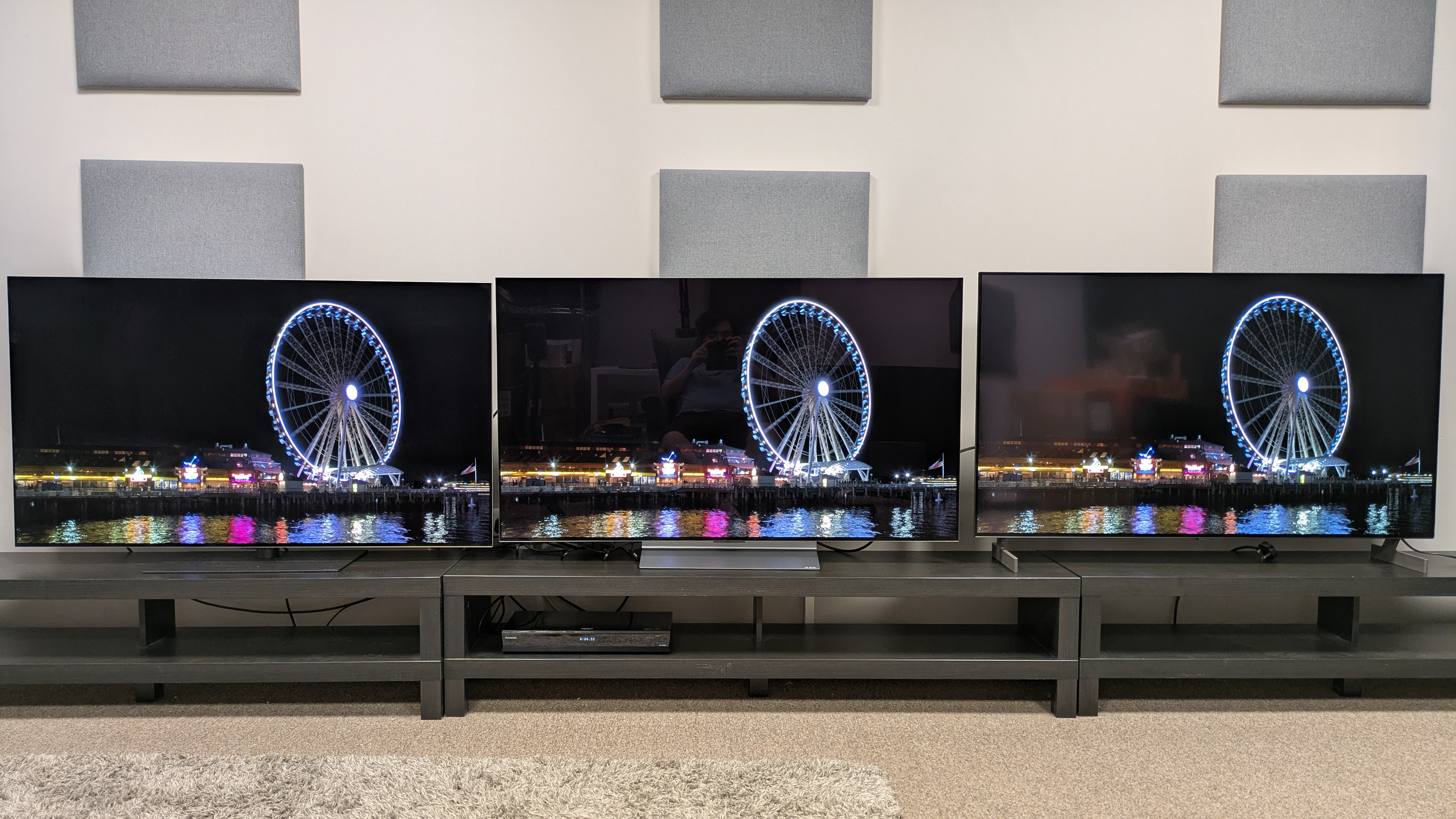 LG G6 (left) vs LG C6 (middle) vs LG B6E (right) showing a ferris wheel at night on screen, in bright conditions. The G6 shows minimal reflections, while the C6 and B6E look reflective
