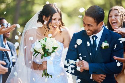 A bride and groom happily walk down the aisle as flower petals are showered on them. 