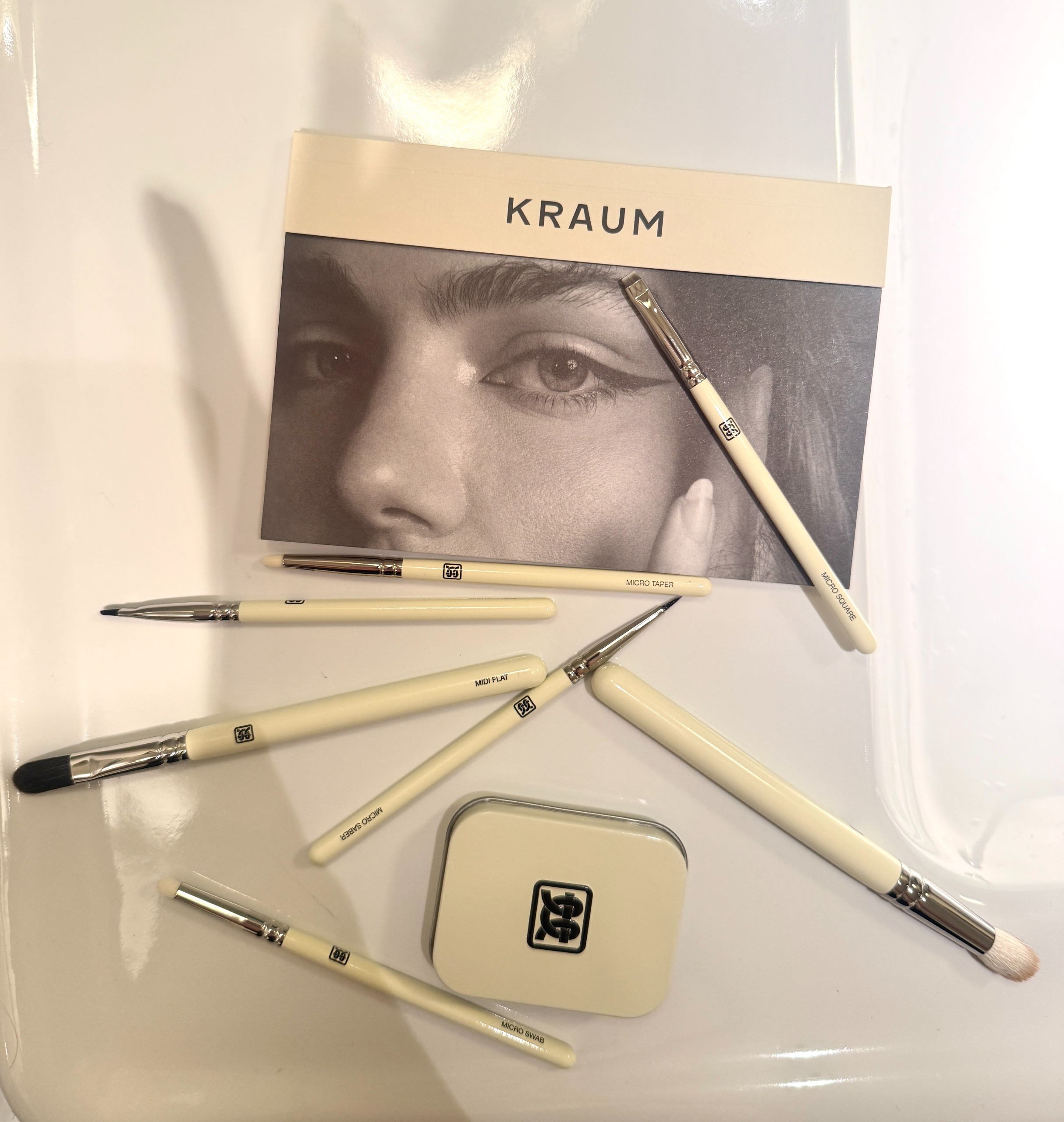 Kraum makeup brushes arranged on a bathroom sink featuring brand&amp;rsquo;s black-and-white packaging and brush soap