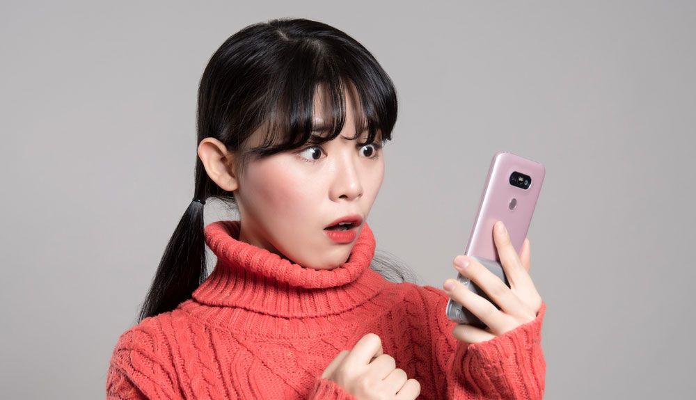 A woman looking at her smartphone in alarm.