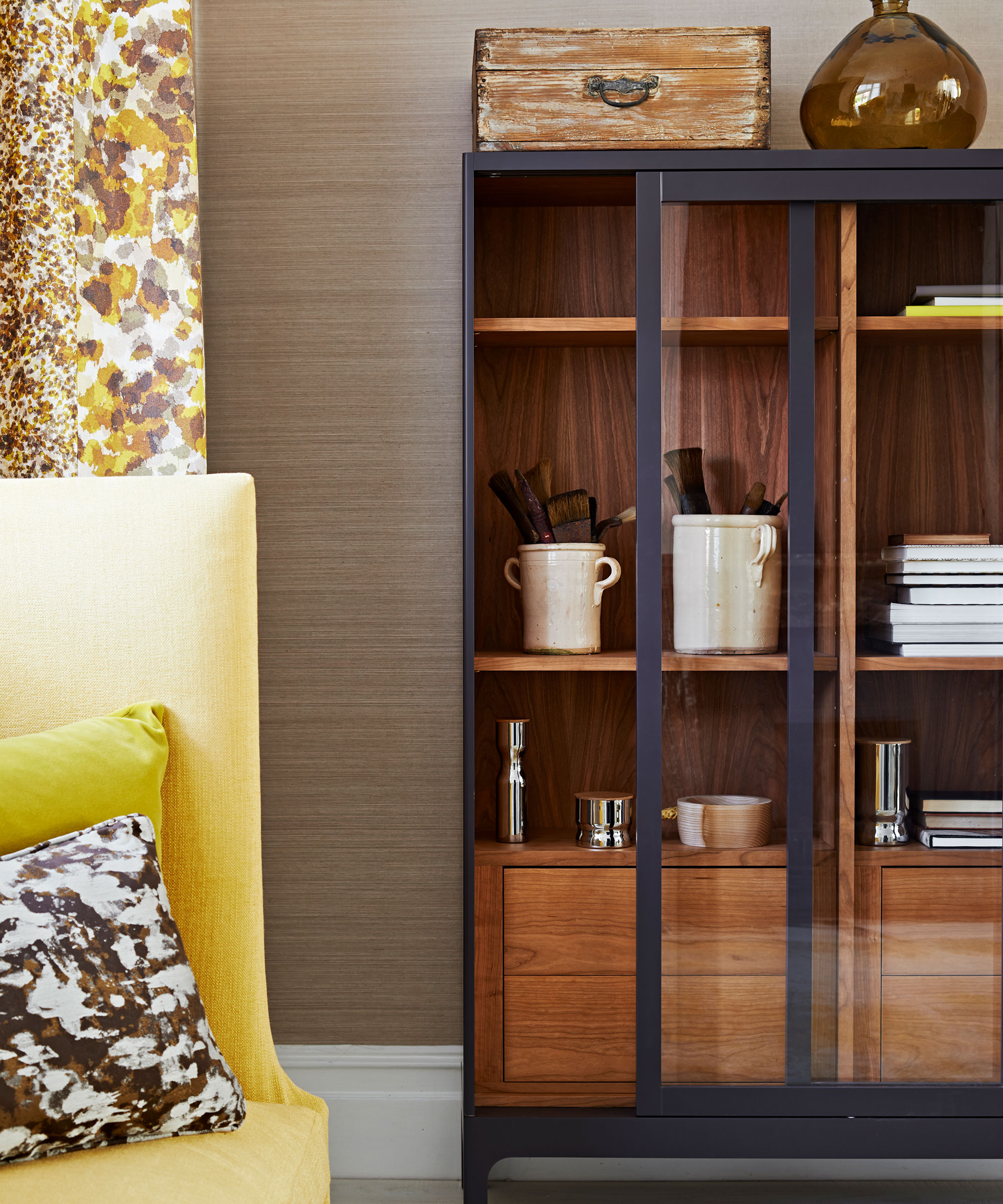 A wooden display cabinet next to a yellow armchair