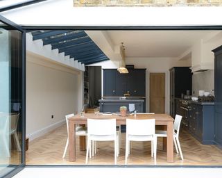 A kitchen extension with parquet flooring and a wooden dining table with white chairs in front of open bifold doors