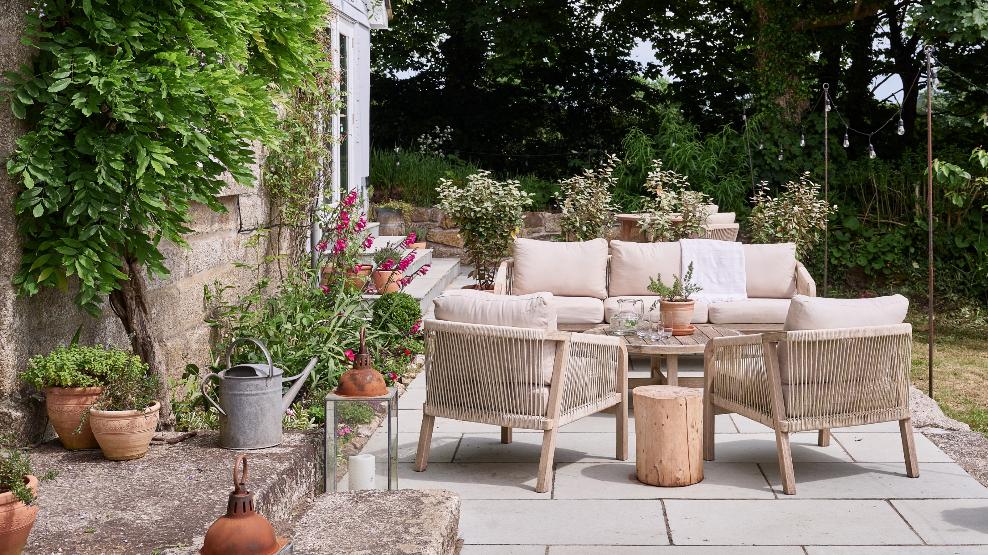A garden with a patio with a wooden garden lounge set with rope detailing