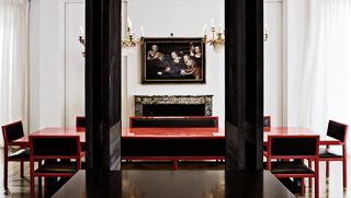 Interior view of a space in a London townhouse designed by Christian Liaigre featuring a large red table, red and black chairs and a fireplace with a painting above