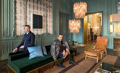 In the living room, Britt Moran (left) and Emiliano Salci sit on one of their own divans, illuminated by vintage Venini chandeliers