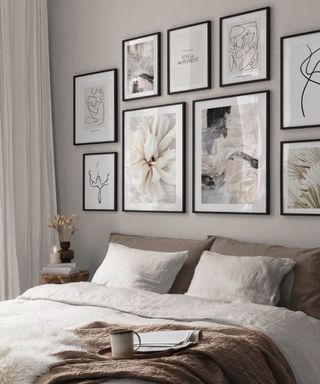 A greige bedroom with a gallery wall with eight floral and line prints and a bed with a bed with white bedding and a gray headboard, and a long white curtain panel to the left
