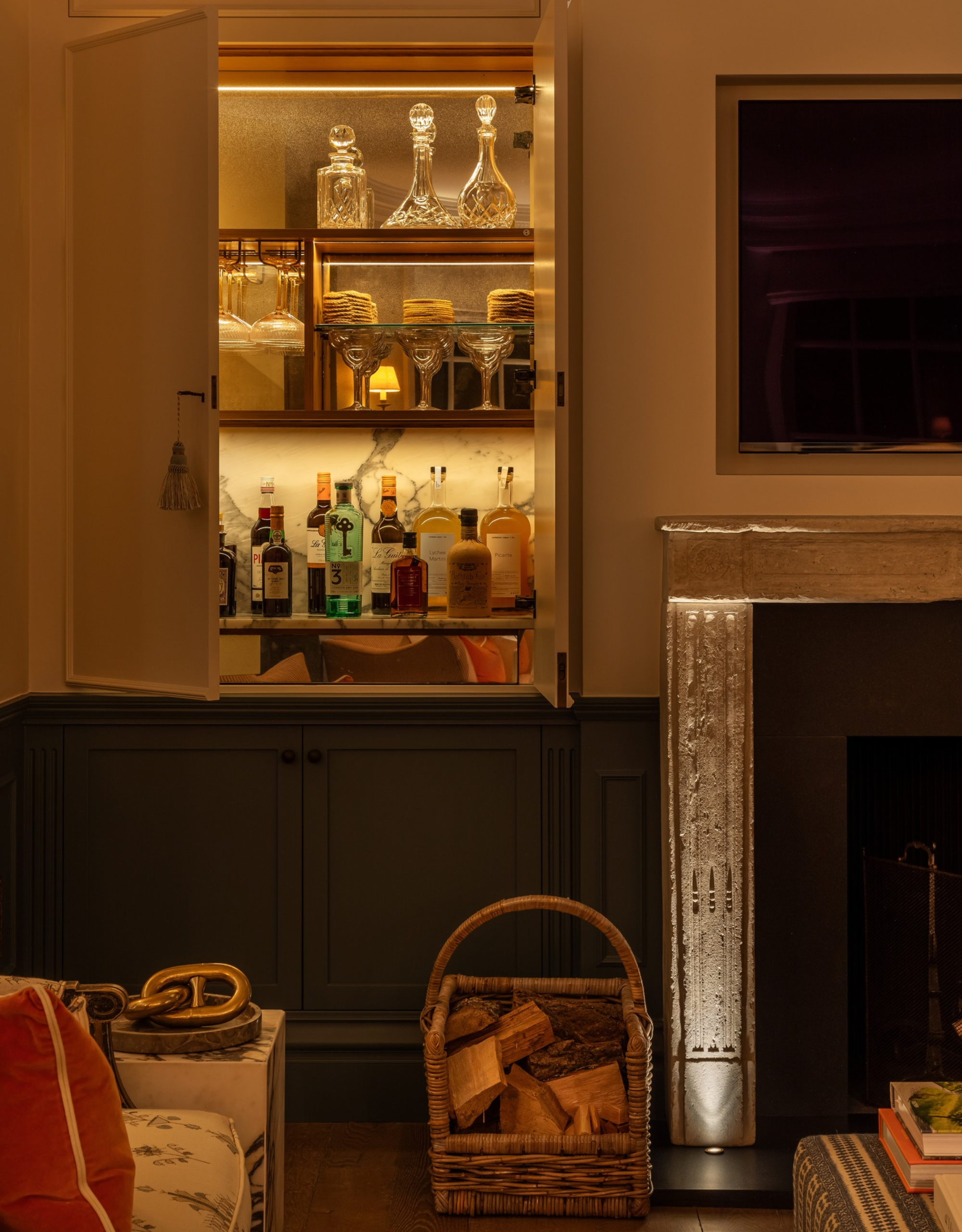 A moodily lit living room with a back lit, hidden bar next to a stone fireplace