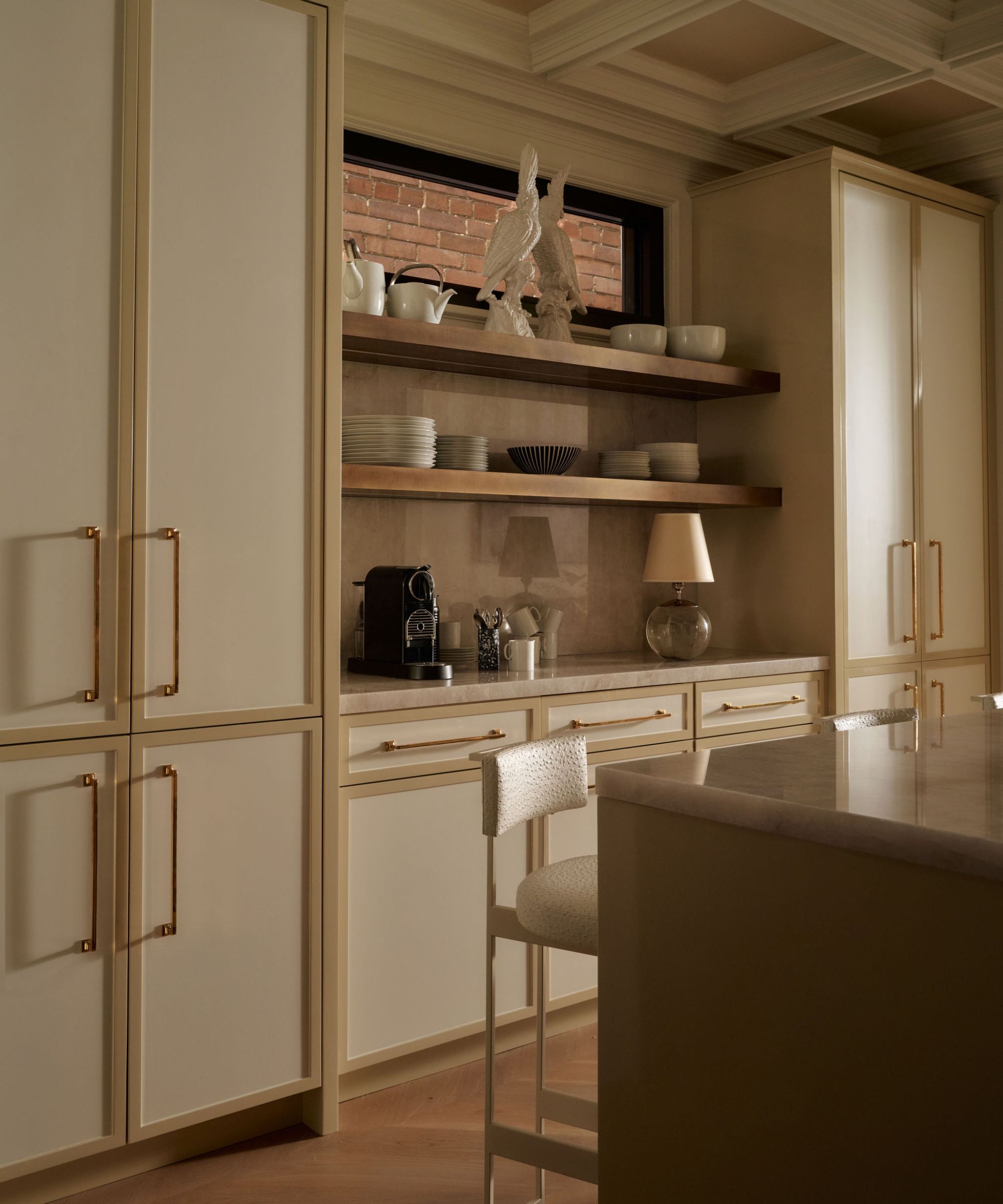 a white and gold kitchen with a modern kitchen island with marble counters, and a built in open shelved bar