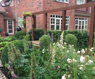 A planting bed filled with cottage garden plants in front of a red brick house