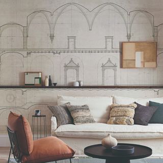 A living room with an architectural mural wallpaper with a cream sofa in front of it and accent chair with a round black coffee table