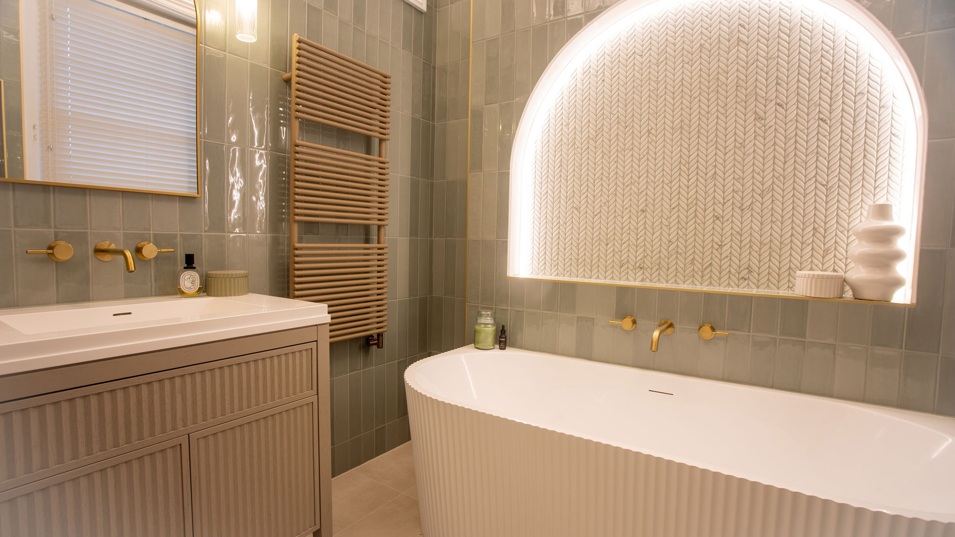 matt brass heated towel warmer in luxury bathroom with backlit alcove and fluted fitted furniture