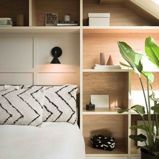 Sleek, wooden recessed shelving compartments surrounding bed, with chevron mono cushions, black geo wall light, and fresh houseplant.
