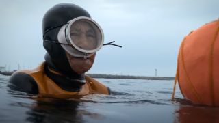 One of the last haenyeo diving women resting aobve the water and next to a buoy in A24's The Last of the Sea Women.