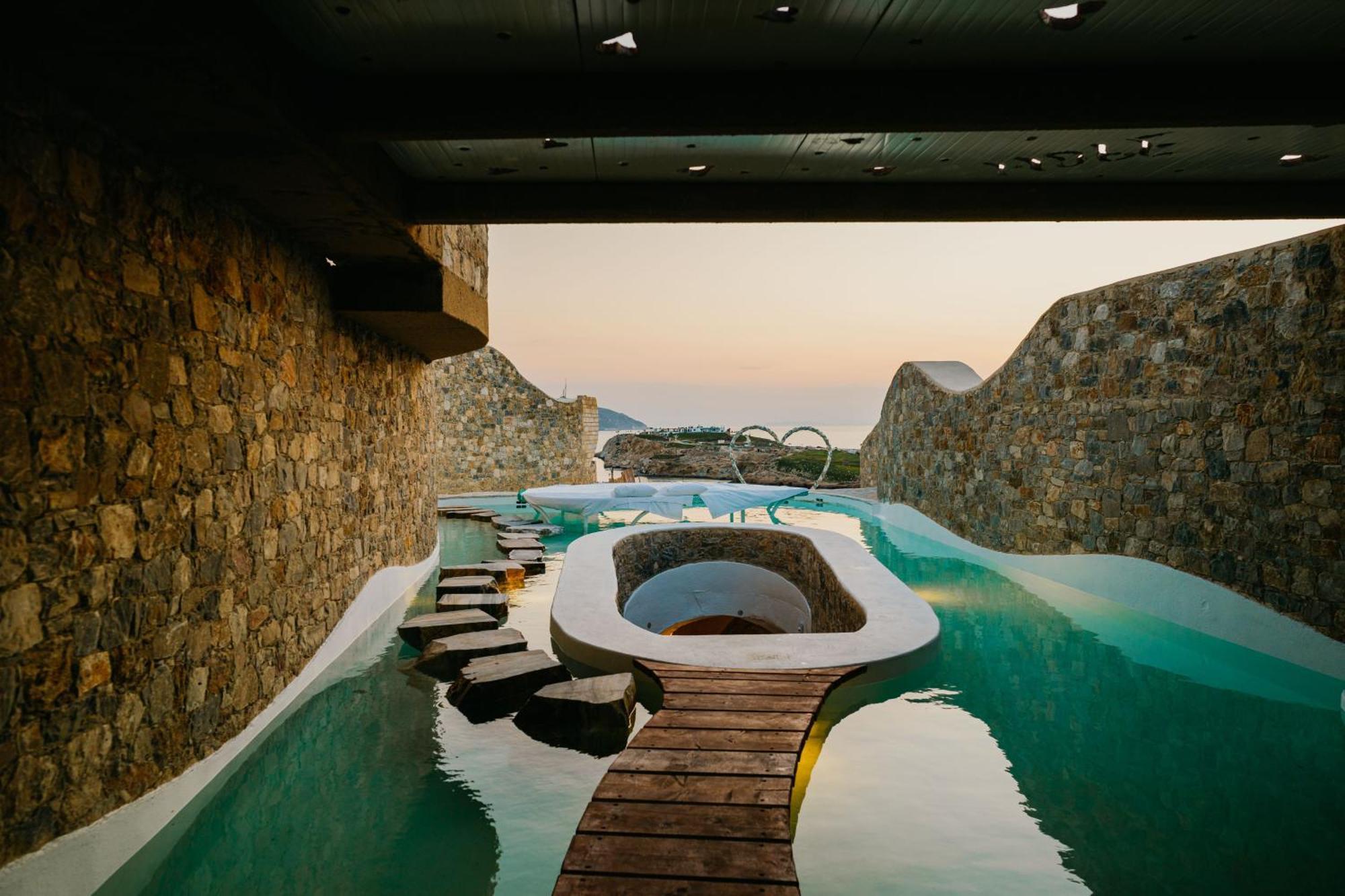 View from the wooden bridge of a winding pool with multiple passageways, slides, and stone-clad holes, carved inside a series of undulating rock walls.