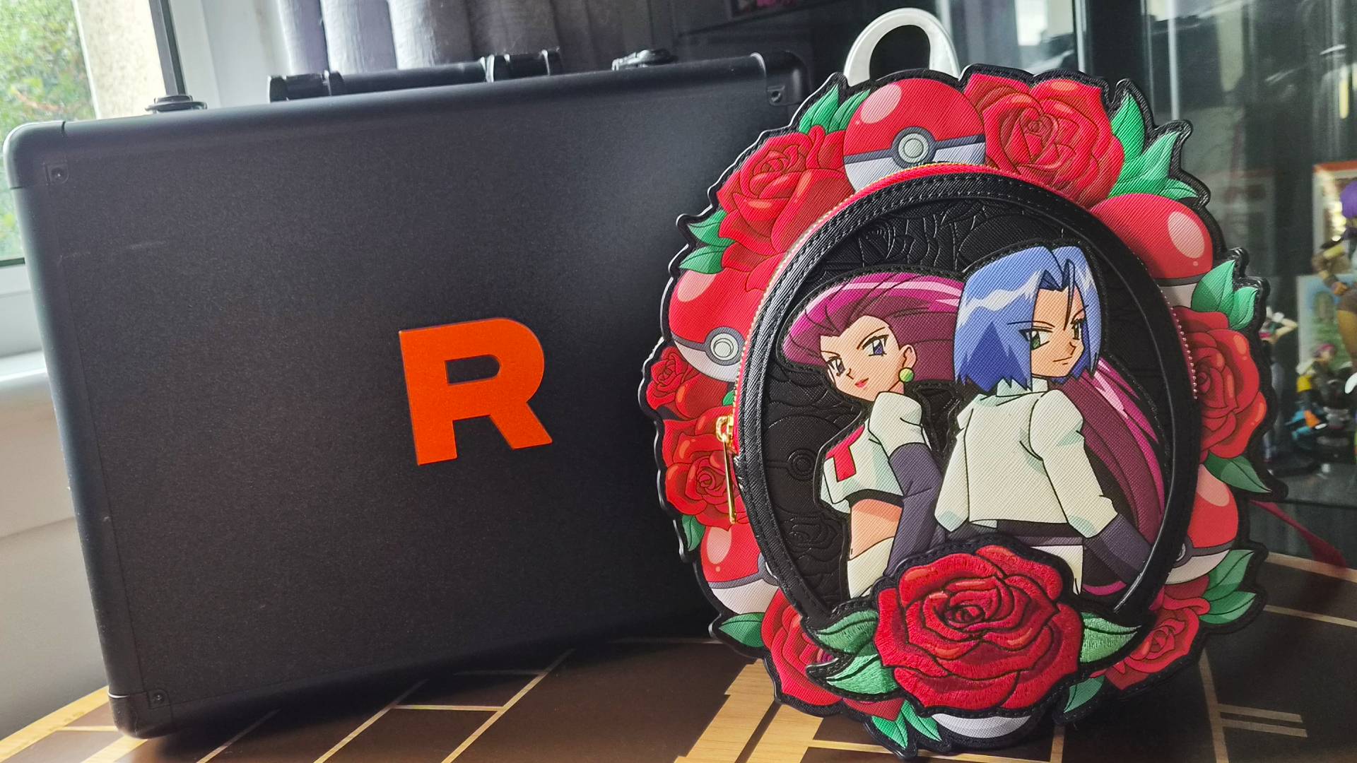Image of the Team Rocket Cameo Mini Backpack sitting in front of a Team Rocket suitcase.