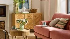 A cosy, warm modern cottage-style lounge with a pink sofa, a small round coffee table and a wooden side table from Argos.