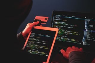 Back view of hooded internet criminal hacking laptop in the dark, stealing credit card details