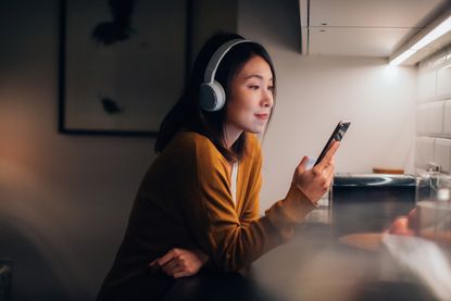Woman listening to podcast on smartphone at home in the evening