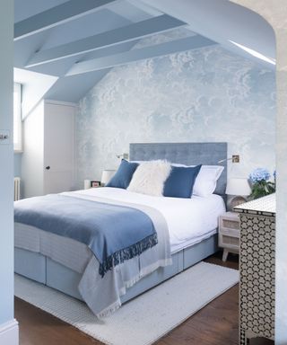 blue bedroom with blue cloud wallpaper, blue button backed bed, hardwood floor, painted blue ceiling and beams