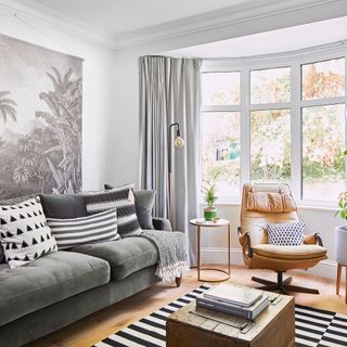 grey living room with large window, grey sofa and leather armchair