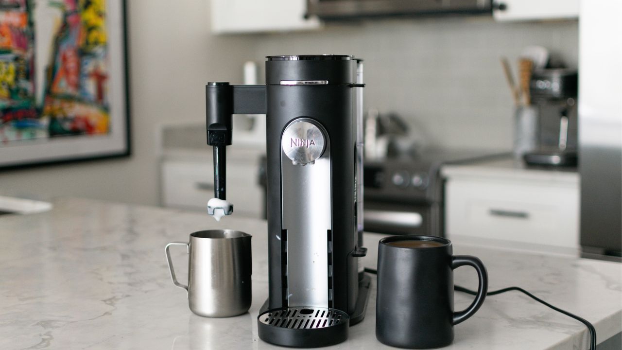 Wide shot of Ninja® PB051 Pods &amp; Grounds Specialty Single-Serve Coffee Maker in Heather Bien&#039;s kitchen on marble worktop with framed wall art in background