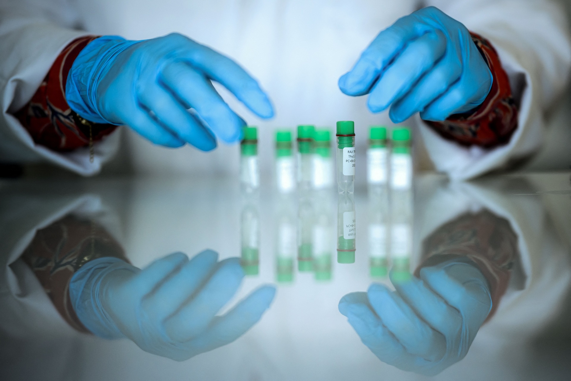 a researcher grabs vials on a reflective tabletop
