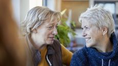 Two older women smile and talk in a restaurant.