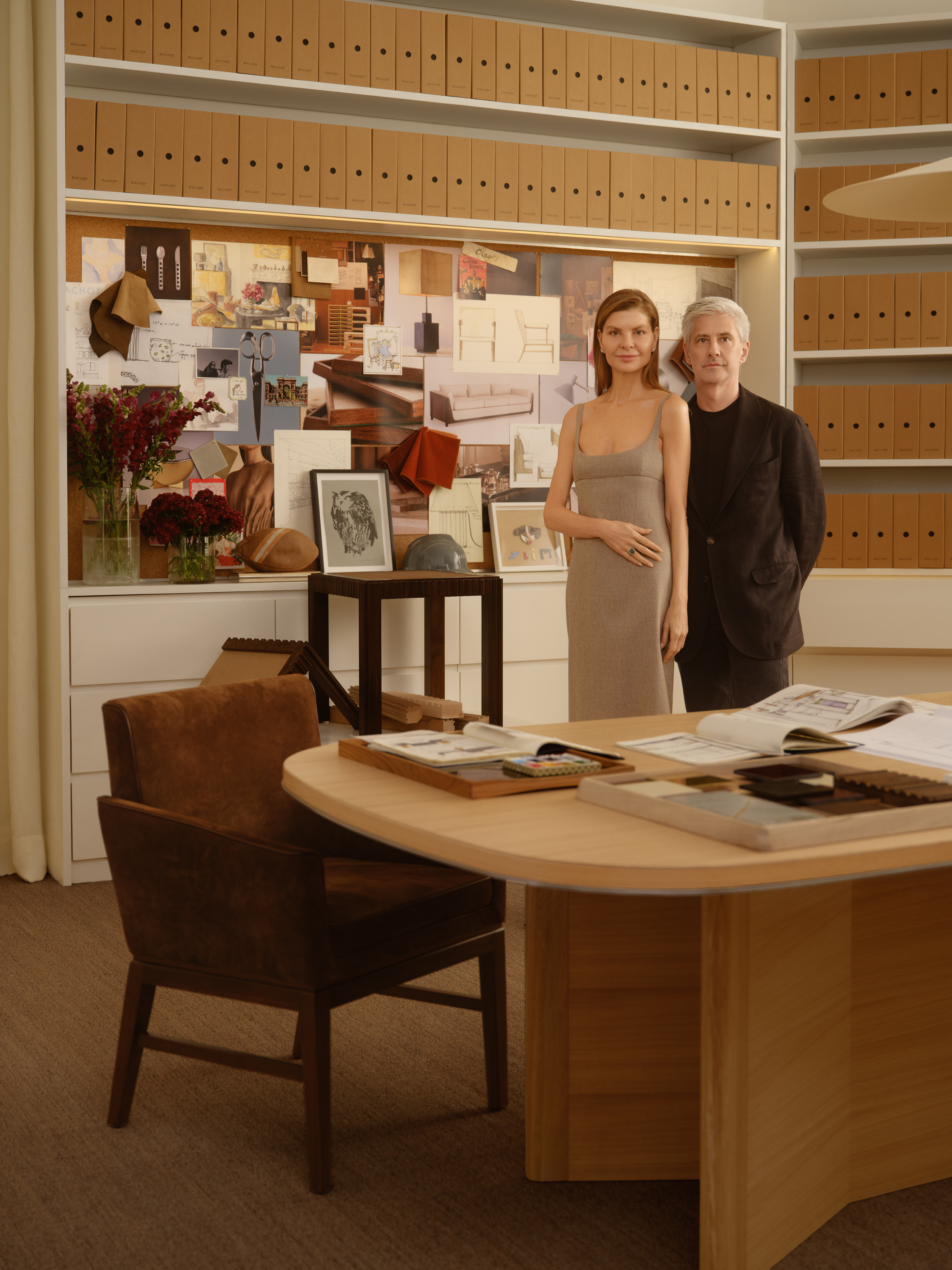 Interior shots of a beige and brown-tinted design atelier decorated with 1970s-inspired furniture designs, pendant lights, collectibles, and plants, and lots of preparatory sketches.