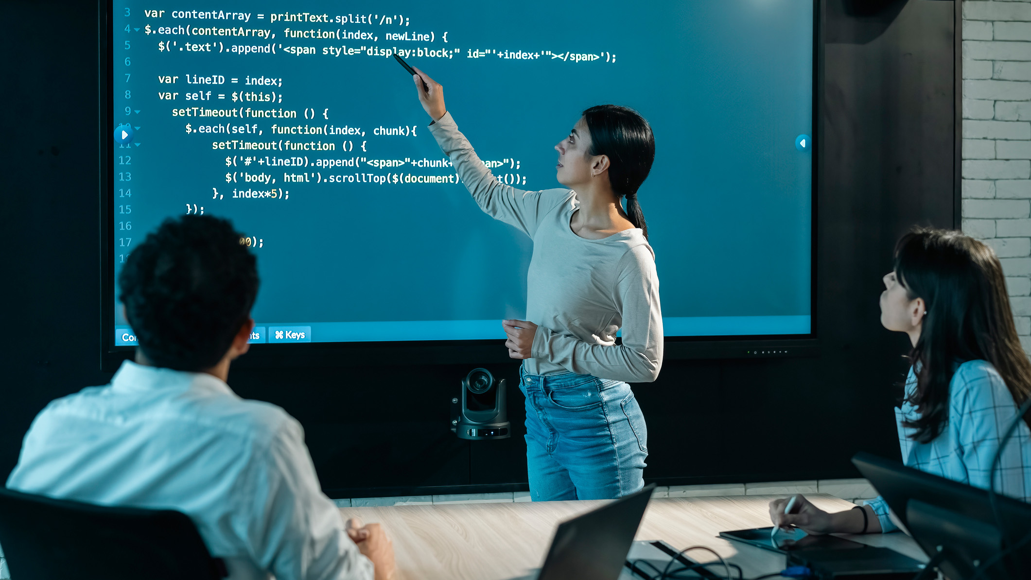 A photo of a young, female software developer presenting code to two colleagues on a conference room screen.
