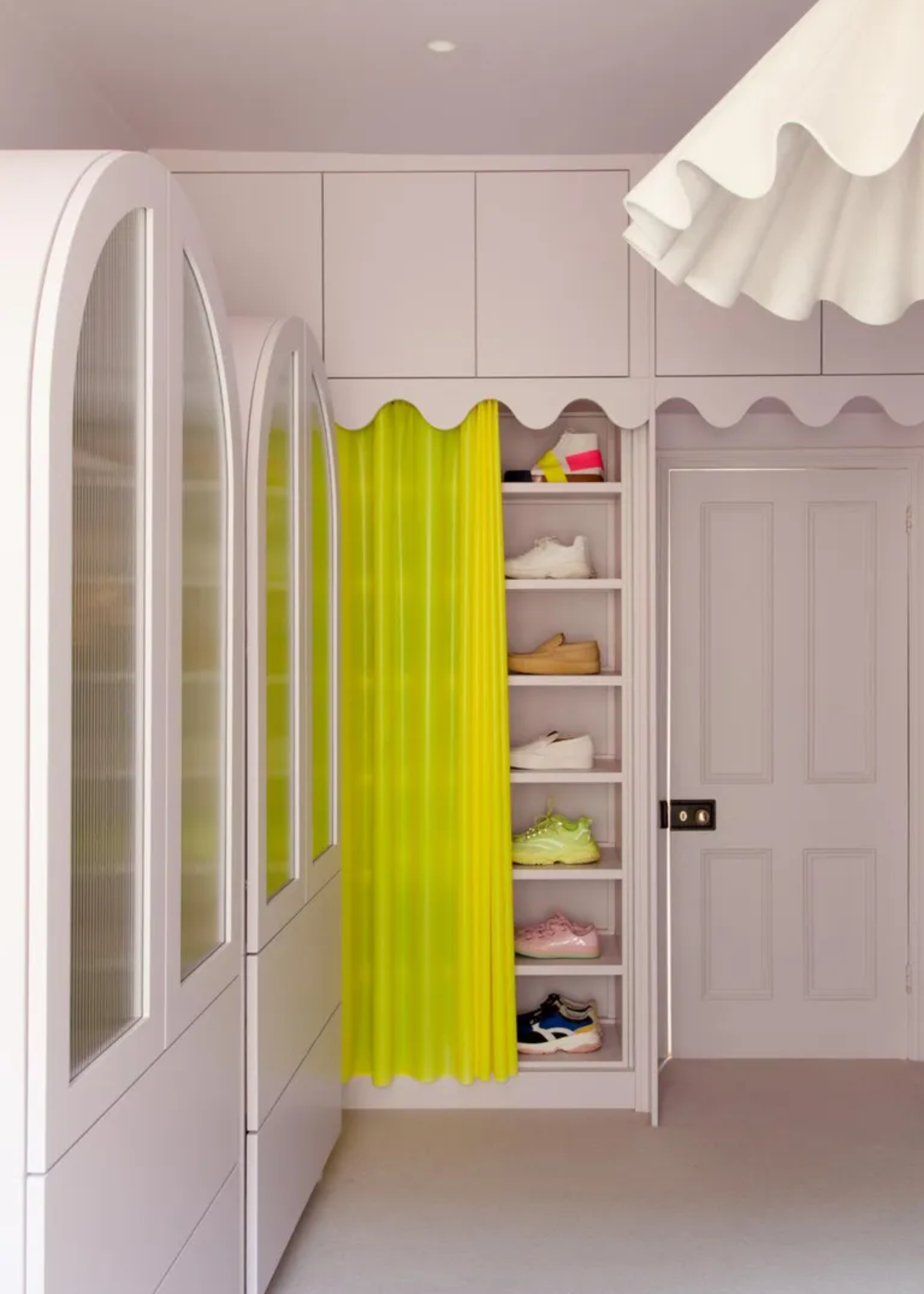 A white wardrobe with a shoe shelf covered by a neon semi-transparent curtain and a wavy ceiling light