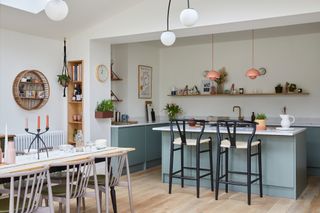 Kitchen-diner with green units, coral pendant lights over island, dining table and chairs, and wooden floor