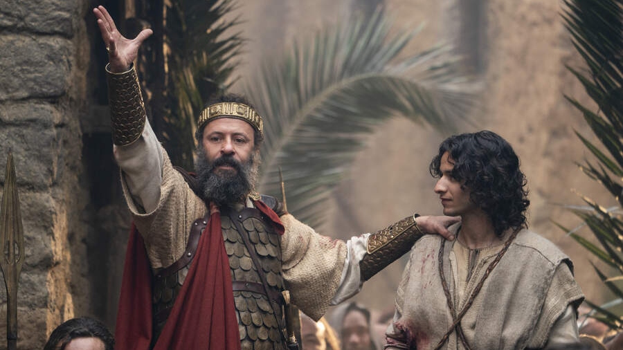 Ali Suliman as King Saul with his right arm outstretched upwards and his left arm on the shoulder of Michael Iskander as David in character in House Of David