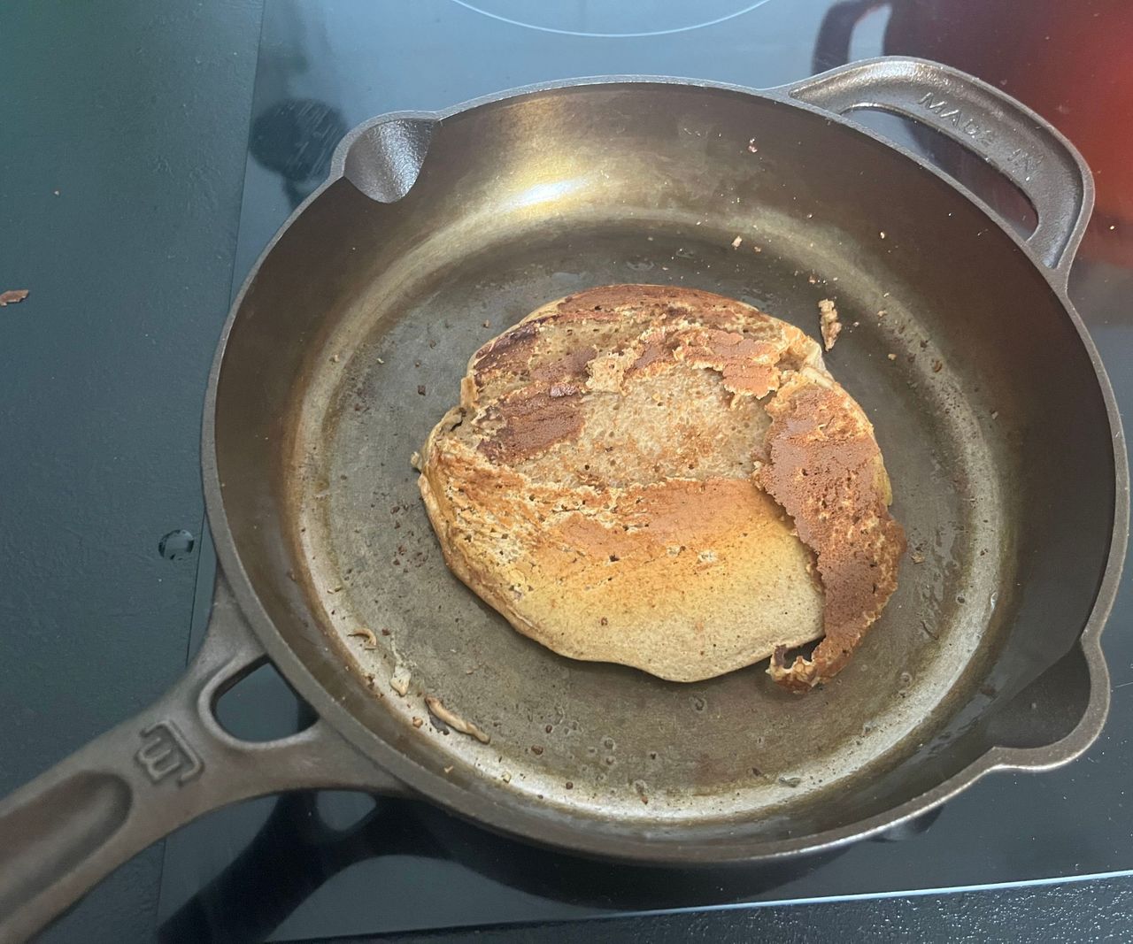 A small bronze colored cast-iron skillet with a broken pancake iside.