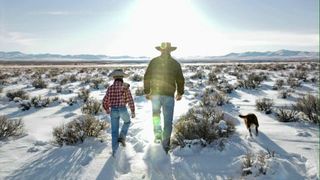 A man and boy in cowboy hats walk through a field towards the sun