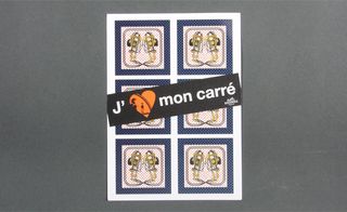 Front view of the Hermès and Colette collaboration invitation pictured against a grey background. The invitation features a repeating image plus white text and an orange heart on a black diagonal strip in the middle of the card