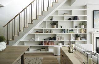 Basement with staircase and bespoke shelving below, table wood floor, rug, console table and sofa