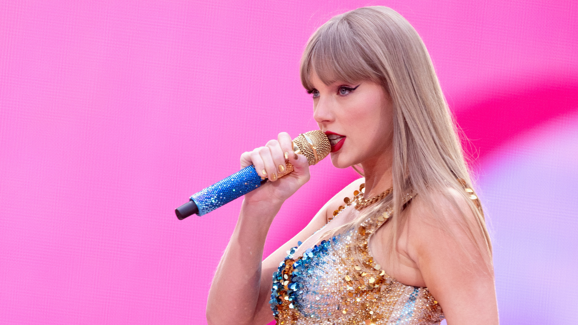 Close-up of Taylor Swift singing, against a pink background, dressed in sequined outfit, at Wembley Stadium on 21 June 2024 on her Eras tour